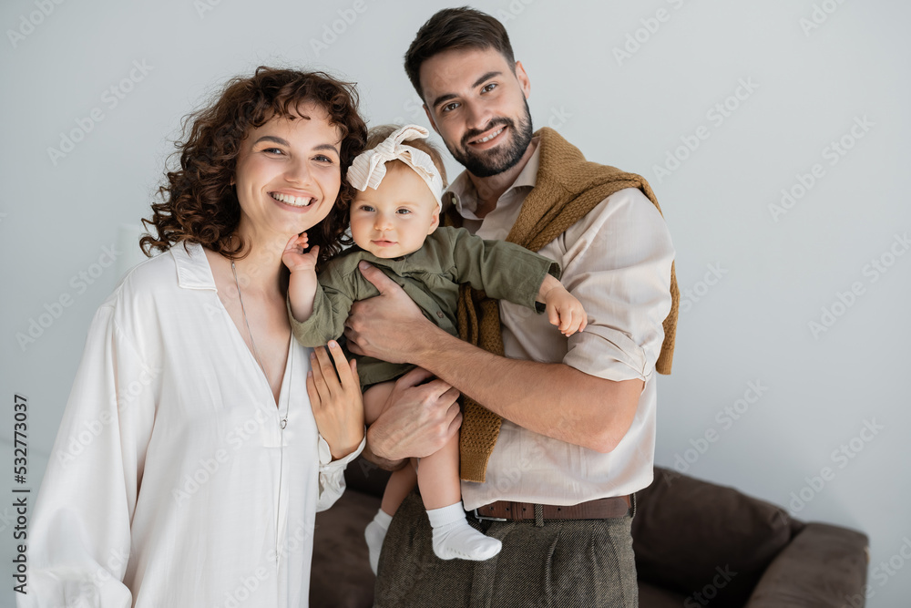positive bearded man holding in arms baby daughter in headband near curly wife. positive bearded man holding in arms baby daughter in headband near curly wife.