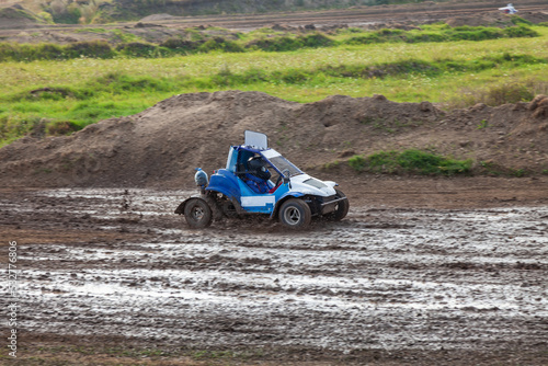 A small sports buggy racing vehicle with a child driving on a rally competition track during weekend training on a warm summer day.