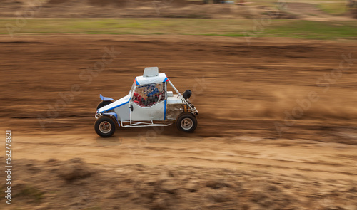 A small sports buggy racing vehicle with a child driving on a rally competition track during weekend training on a warm summer day.