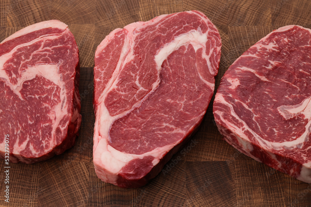 Three raw ribeye beef steaks on cutting board