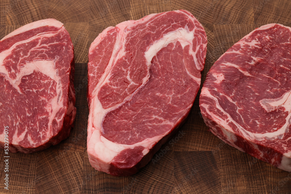 Three raw ribeye beef steaks on cutting board Three raw ribeye beef steaks on cutting board