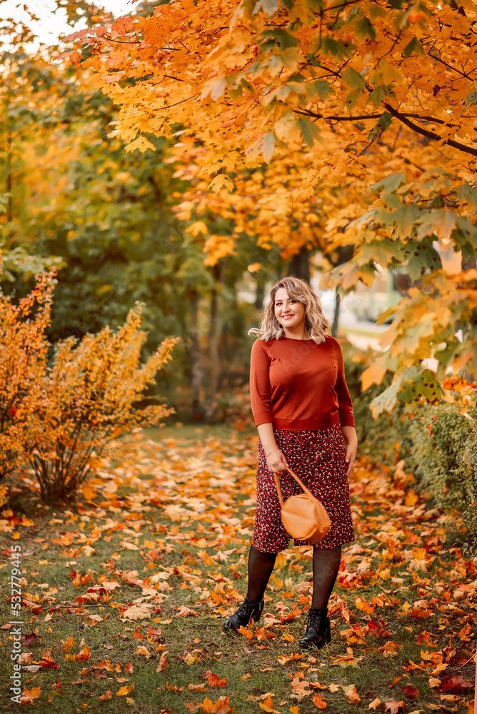 young stylish plus-size woman walks in an autumn park. Tosses leaves. A beautiful smiling girl in a brown suit on a background of golden leaves young stylish plus-size woman walks in an autumn park. Tosses leaves. A beautiful smiling girl in a brown suit on a background of golden leaves