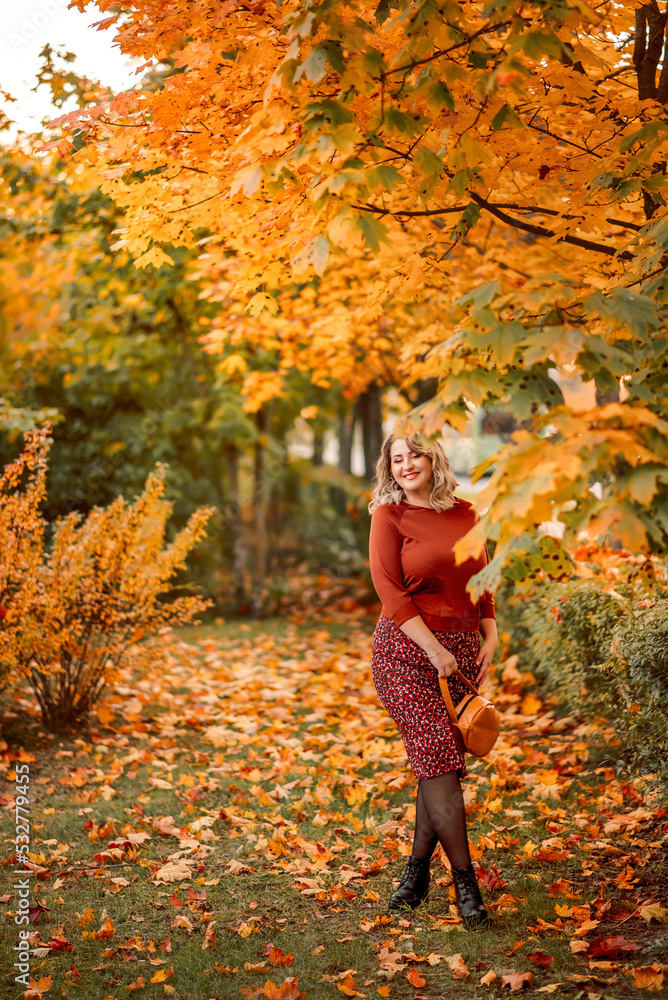 young stylish plus-size woman walks in an autumn park. Tosses leaves. A beautiful smiling girl in a brown suit on a background of golden leaves young stylish plus-size woman walks in an autumn park. Tosses leaves. A beautiful smiling girl in a brown suit on a background of golden leaves