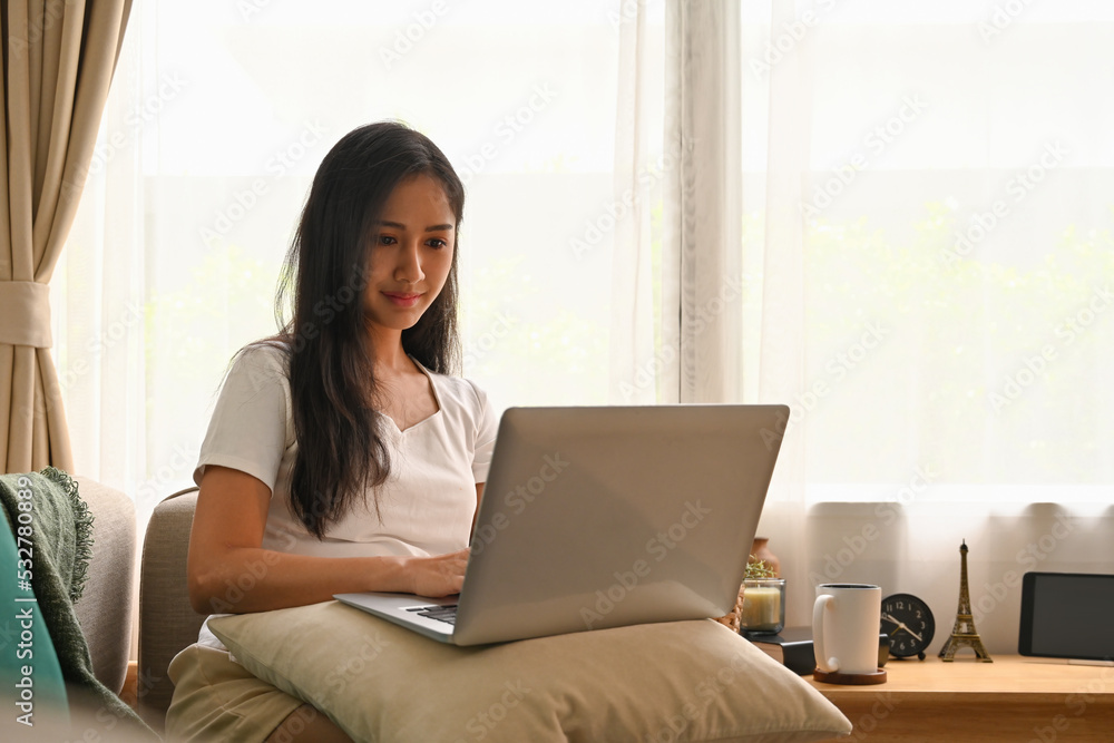 Domestic life concept at home with Asian female using laptop while sitting on the sofa in the living room. Domestic life concept at home with Asian female using laptop while sitting on the sofa in the living room.