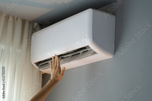 Female owner of apartment stretches hand to check operating air conditioner and catch stream of warm air. Person wants to make flat warm turning on modern device. Landlady enjoys caring about house photo