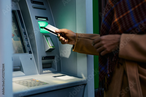 Close up of black woman using credit card while withdrawing cash at ATM. photo