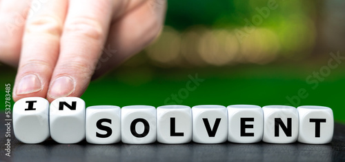 Hand turns dice and changes the word solvent to insolvent. photo