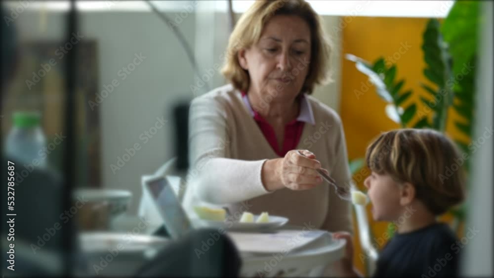 Grandmother feeding grandson at lunch time in terrace while in conversation. Candid grandma feeds small boy fruit Grandmother feeding grandson at lunch time in terrace while in conversation. Candid grandma feeds small boy fruit