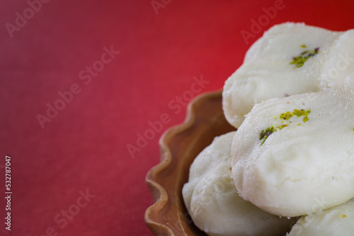 Bengali traditional sweet sandesh served on a clay plate for celebration of indian festivals. white jolbhora or talsaash sandesh, made of cottege cheese.close-up shot in red background.