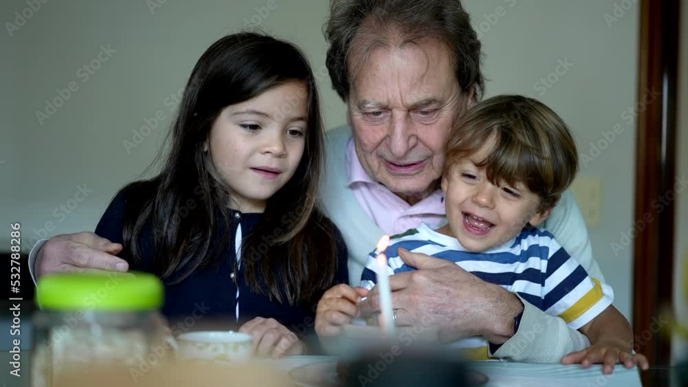 Happy senior blowing birthday candle with children. Grandfather celebrates anniversary with grandchildren. Generational family concept Happy senior blowing birthday candle with children. Grandfather celebrates anniversary with grandchildren. Generational family concept