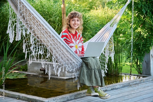 Portrait of teenage girl with laptop sitting in hammock in backyard photo