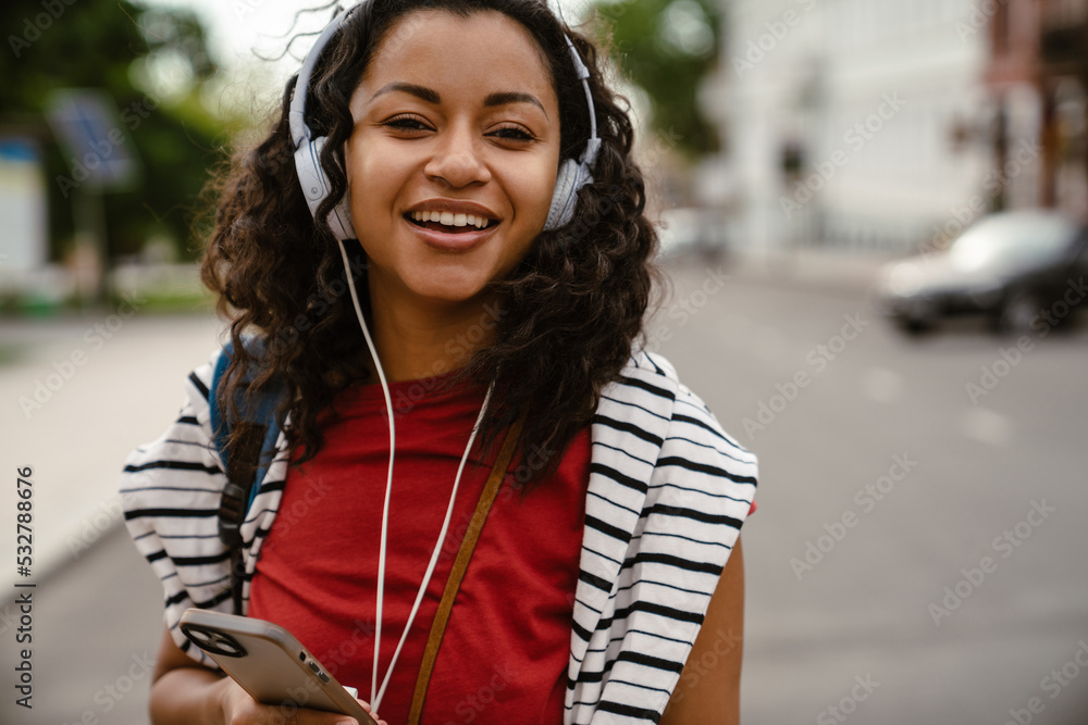 Young woman in headphones using mobile phone while walking outdoors Young woman in headphones using mobile phone while walking outdoors