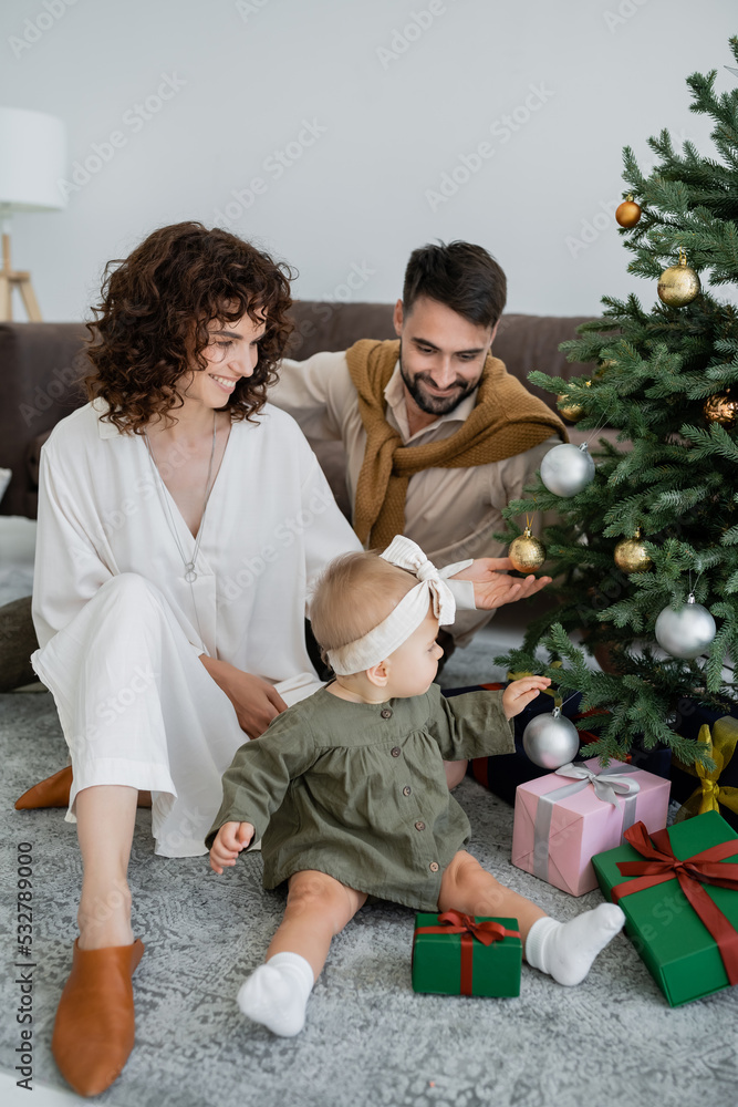 happy family with infant baby girl sitting near christmas tree with presents. happy family with infant baby girl sitting near christmas tree with presents.