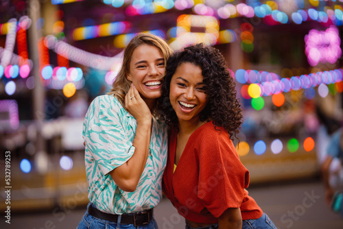 Young multiracial women laughing and hugging in attraction park