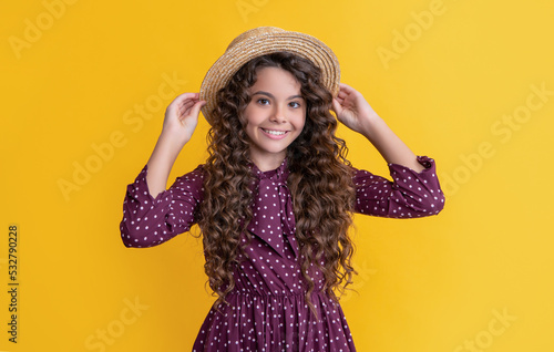 happy child in straw hat with long brunette curly hair on yellow background