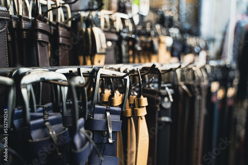 different kinds of leather colored belts for jeans and suits hanging by the buckle in clothes store display