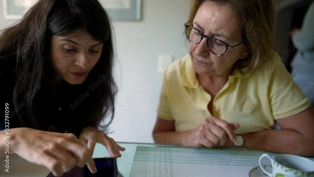 Adult daughter explaining information to older mother using cellphone device. Person showing smartphone to senior woman Adult daughter explaining information to older mother using cellphone device. Person showing smartphone to senior woman