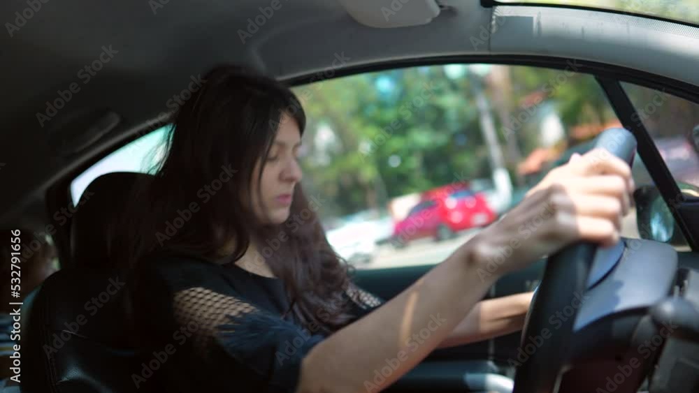 Woman sitting inside car waiting to enter road holding steering wheel. 30s female person driver looking at left rear view mirror Woman sitting inside car waiting to enter road holding steering wheel. 30s female person driver looking at left rear view mirror