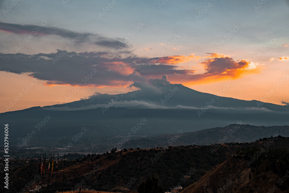 Idyllic view of Mount Etna emitting smoke with sky in background. Vibrant orange clouds covering volcanic mountain peak. Picturesque view of famous tourist attraction during sunset.