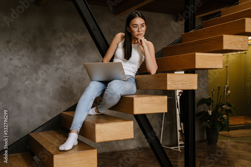 Young asian woman working with laptop while sitting on stairs