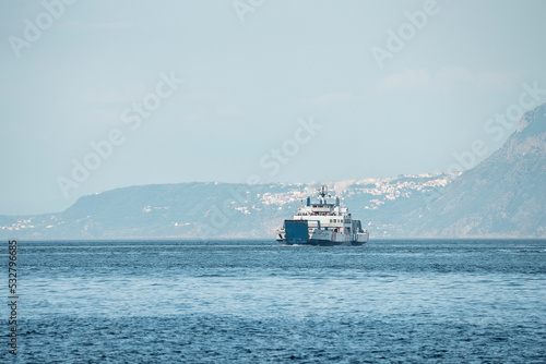 Messina, Sicily, Italy. August 26, 2022. Ship moving on Messina strait. Nautical vessel floating at Mediterranean port against mountain in ancient city with sky in background.