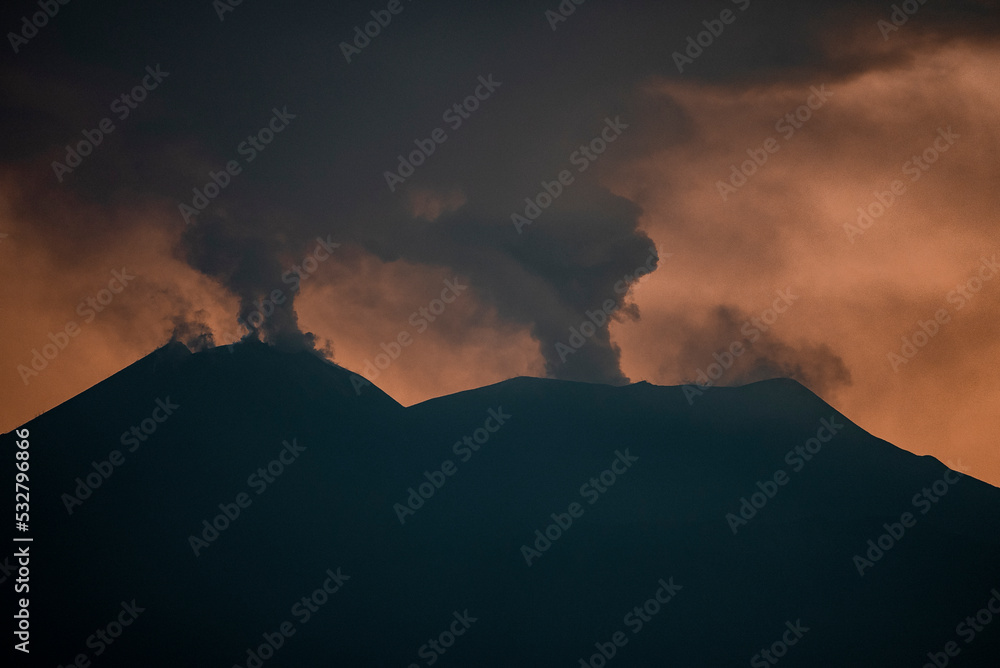 Picturesque view of smoke emitting from volcanic Mount Etna. Atmospheric clouds covering majestic mountain peak at twilight. Beautiful scenery of famous tourist attraction during sunset.