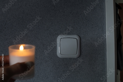 Frau hält Kerze in der Hand während einer Stromausfalls. Im Hintergrund ist ein Lichtschalter