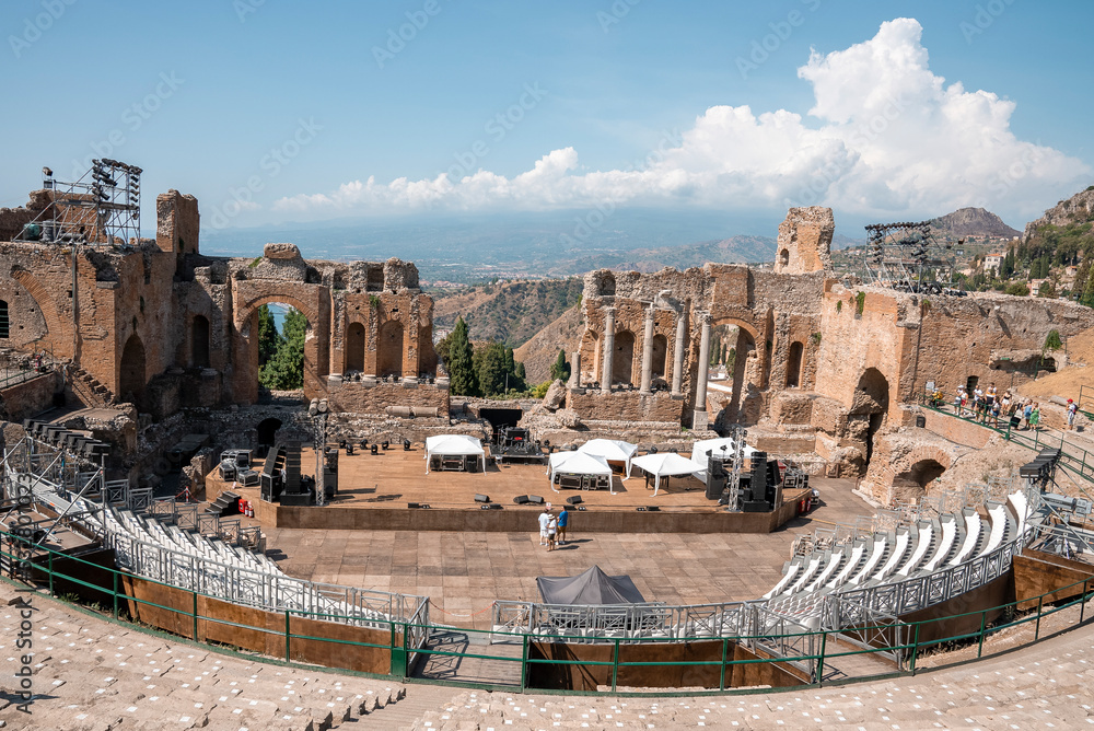 Taormina, Sicily, Italy. August 26, 2022. Tourists exploring old ruins of ancient Greek theater. People visiting famous attraction. They are enjoying summer vacation at Giardini Naxos bay.