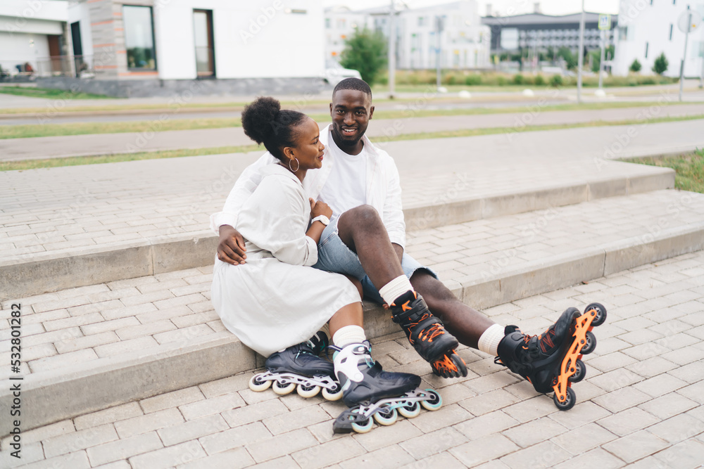 African American couple in inline skates sitting on pavement stairs