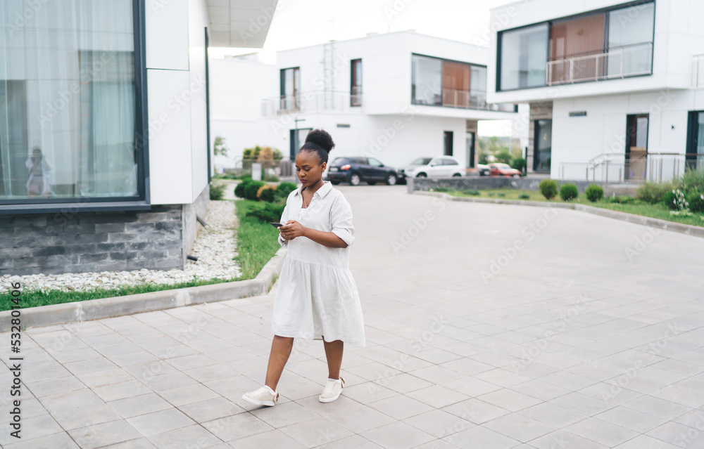 Black woman walking with smartphone on street