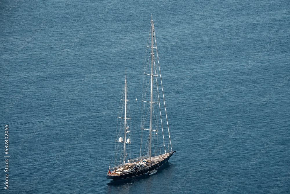 High angle view of yacht with big mast moving on sea. Nautical vessel at beautiful Mediterranean seascape. Scenic view of blue ocean at Italian coast.