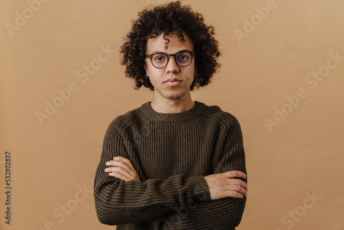 Foto Young handsome curly boy in glasses with folded arms