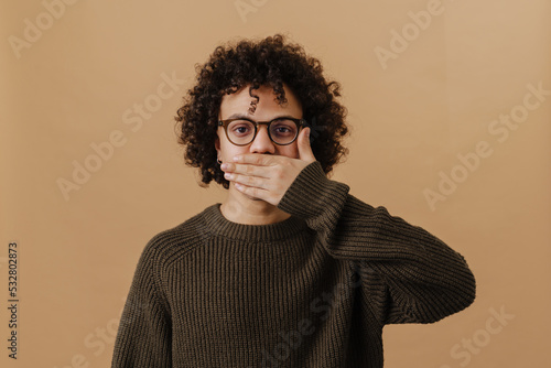 Young handsome curly boy in glasses covering his mouth