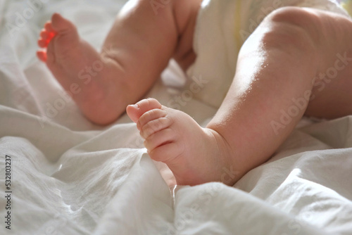 Baby Legs Close up on White Blanket. Healthy Newborn Feet. Warm Sunlight. Beautiful Shot of Infant's Small Feet on a Light Background. Early age children development. Authentic Candid Lifestyle.