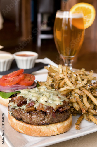 Burger with applewood smoked bacon and melted bleu cheese on a homemade bun. Lettuce, tomato and onion, served with seasoned french fries and a glass of beer. Vertical Photo. 