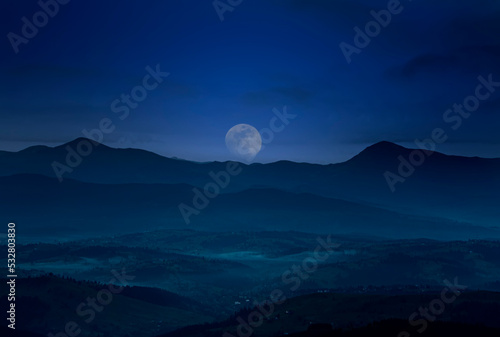 Silhouettes of mountain peaks and full moon. gloomy photo