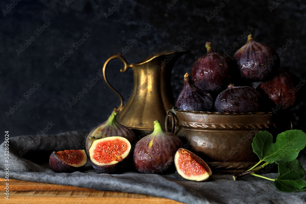 Fresh fig fruits in vintage bronze pot with cut pieces against dark background - dark and moody photography