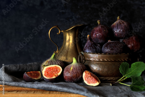 Fresh fig fruits in vintage bronze pot with cut pieces against dark background - dark and moody photography