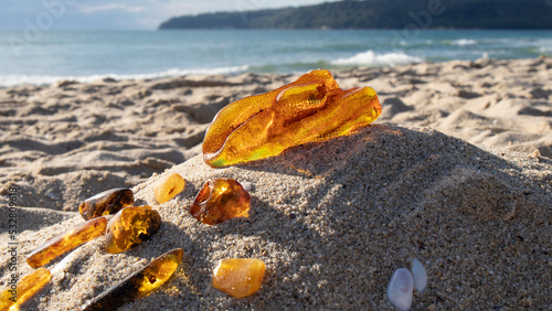 Transparent orange Baltic amber stone on a sand against the sea. Ancient fossil. Material for jewelers. 