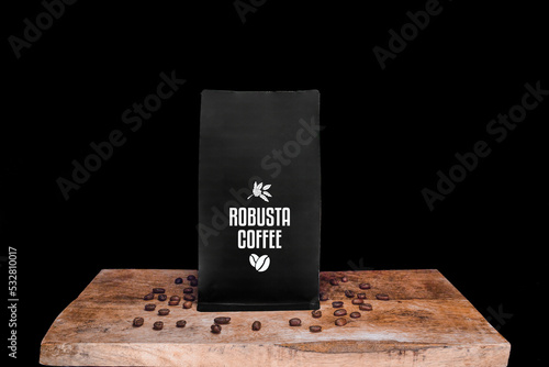 Robusta coffee beans and black package on wooden board with black isolated background