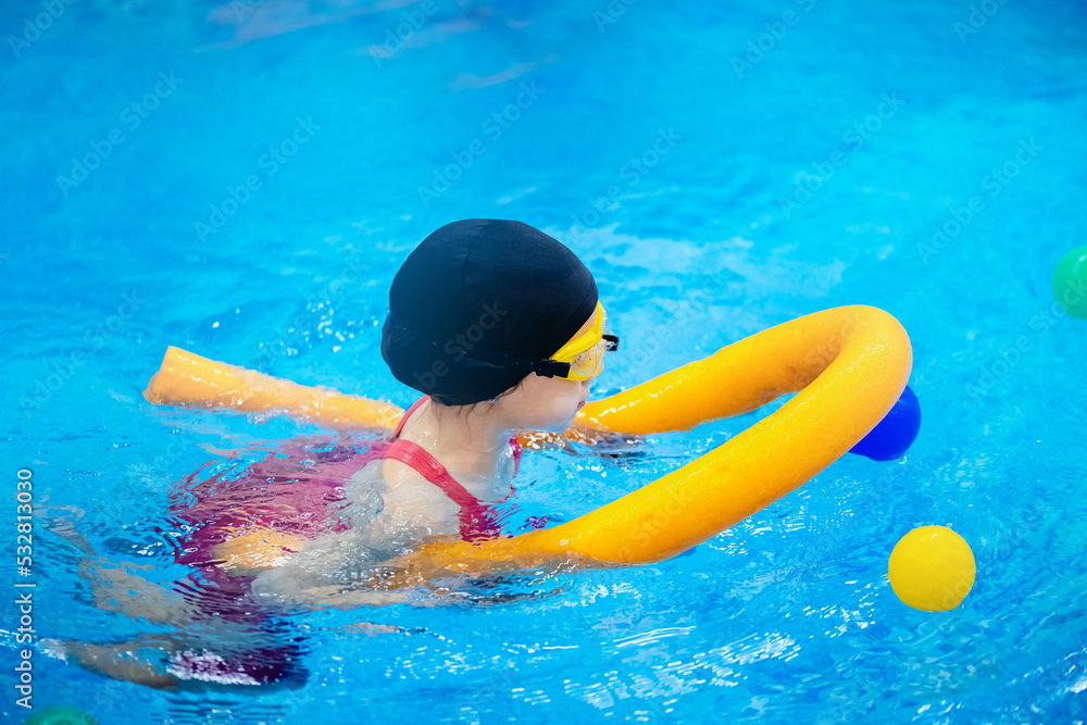 Happy little kid girl learning to swim with pool noodle with coach woman, top view
