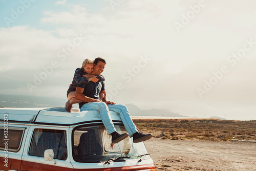 Photo Young couple of traveler enjoy van life vehicle travel adventure together hugging and loving sitting on the roof of the classic camper