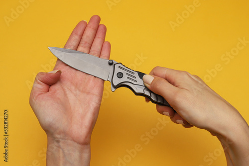 Folding knife in a female hand on an orange background. Close-up