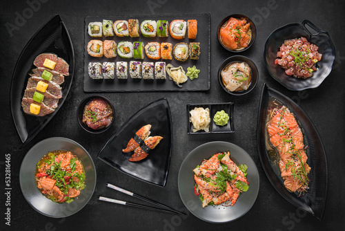Japanese cuisine sushi rolls and sashimi set on a dark stone background. Top view.