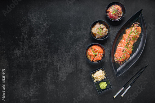Sashimi set with wasabi, ginger and chopsticks on a dark stone background