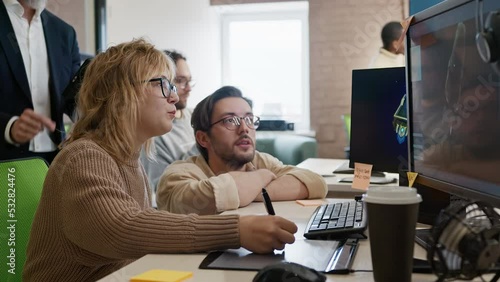 European woman, Caucasian male artist and CEO of company discuss the 3D model in a computer game and application development studio among other team members.