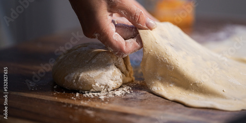 Female hands stretching and pulling homemade vegan pastry dough on domestic dining table