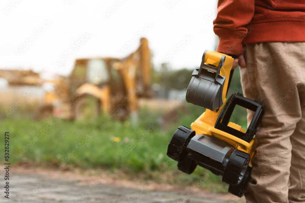 Child with excavator near construction site, dreams to be an engineer. Little builder. Education, and imagination, purposefulness concept Child with excavator near construction site, dreams to be an engineer. Little builder. Education, and imagination, purposefulness concept