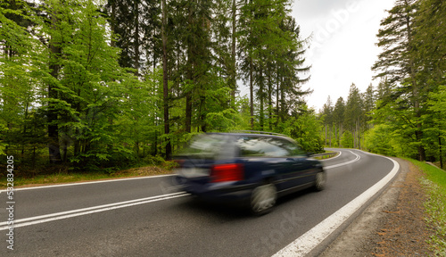 A winding mountain road through a green forest with a car riding © ptyszku