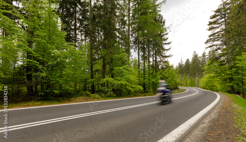A winding mountain road through a green forest with a motorcyclist riding
